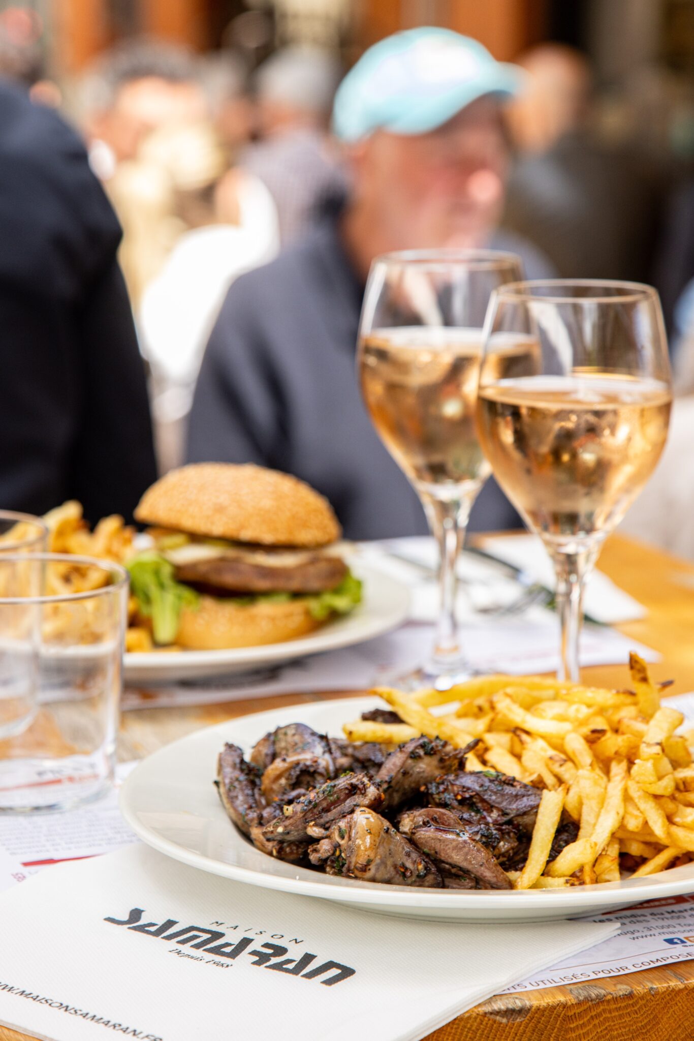 table en terrasse avec assiette de cœurs de canard et burger de canard avec des frites fraiches et des verres de vin